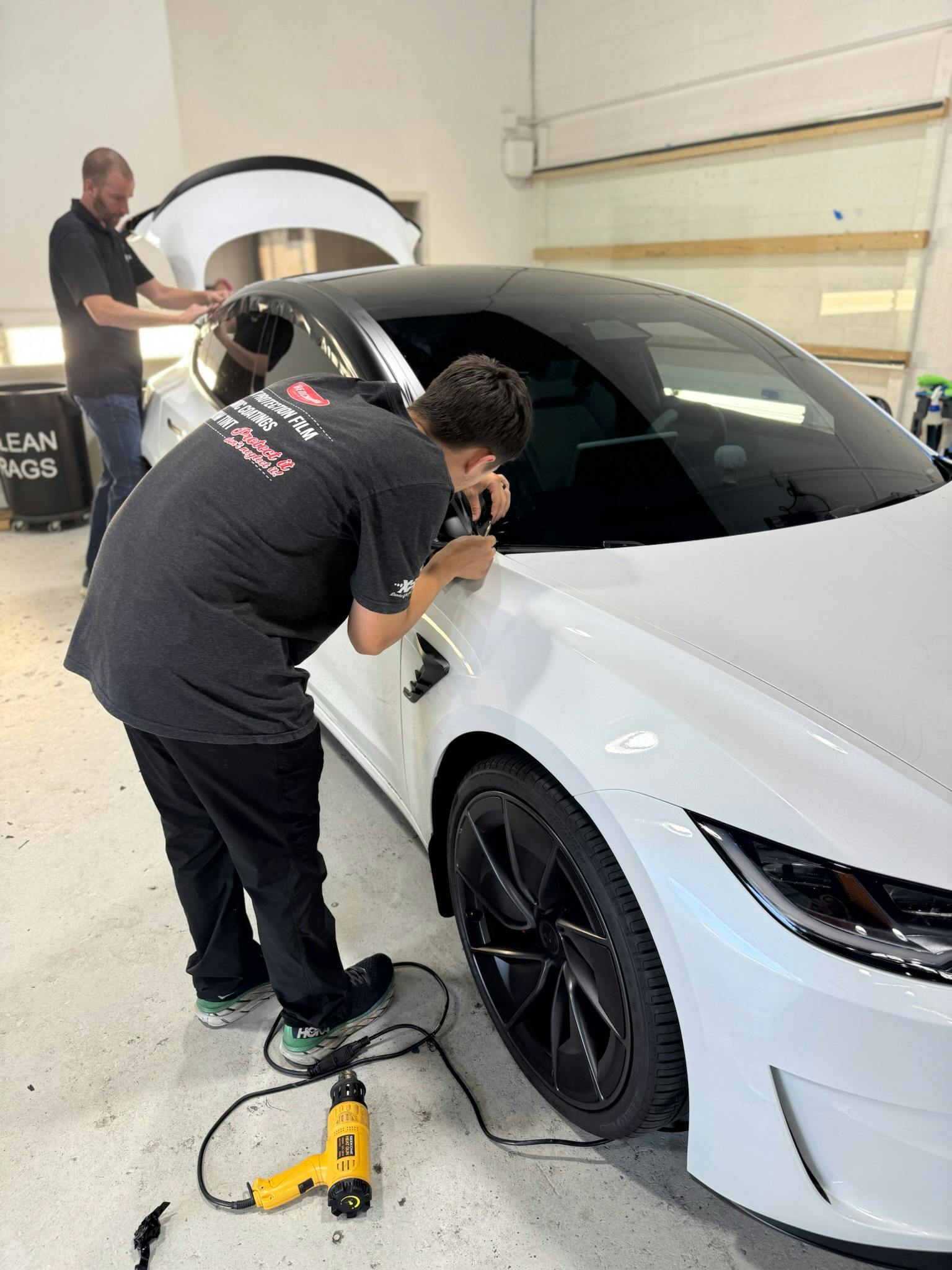 Benchmark Auto Salon installers applying XPEL paint protection film to a white Tesla