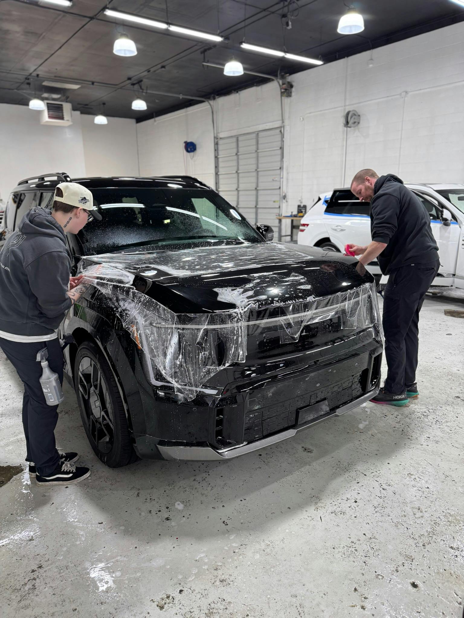 Two technicians installing PPF on a black Kia EV9