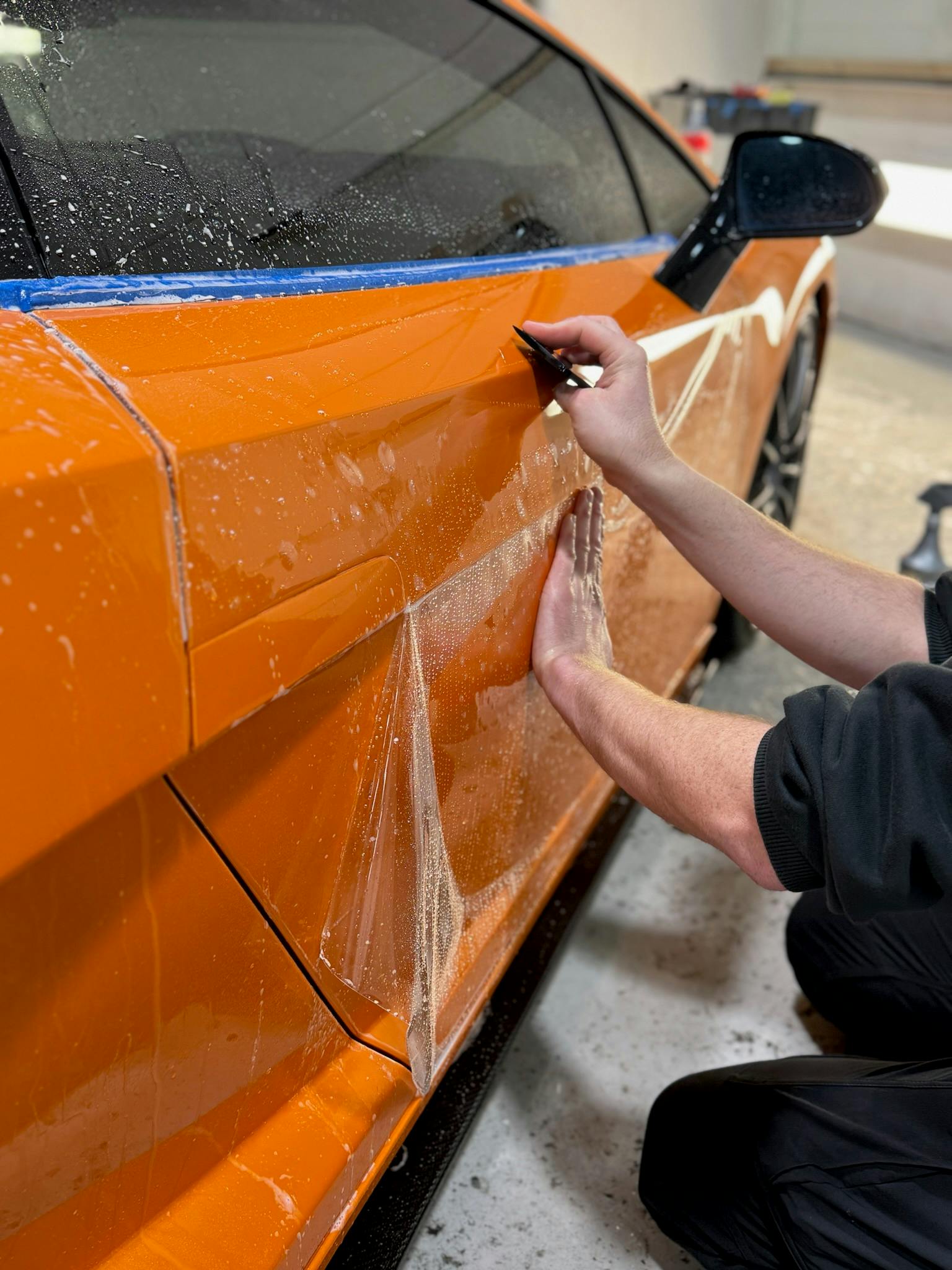 Technician trimming paint protection film on an orange sports car door panel