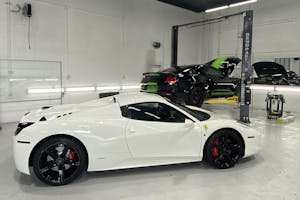 Spacious, well-lit automotive garage featuring a sleek white Ferrari with a black roof, positioned in the foreground.