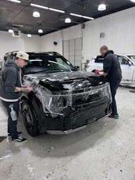 Technicians installing paint protection film on the front of a black SUV at Benchmark Auto Salon