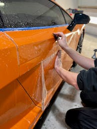 Technician applying paint protection film to the door of an orange Lamborghini Huracán