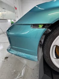 Installing paint protection film on the front bumper of a turquoise Porsche sports car