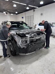 Technicians installing paint protection film on the front of a black Kia EV9 SUV
