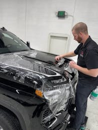 Applying clear paint protection film to the front bumper of a black SUV for rock chip protection