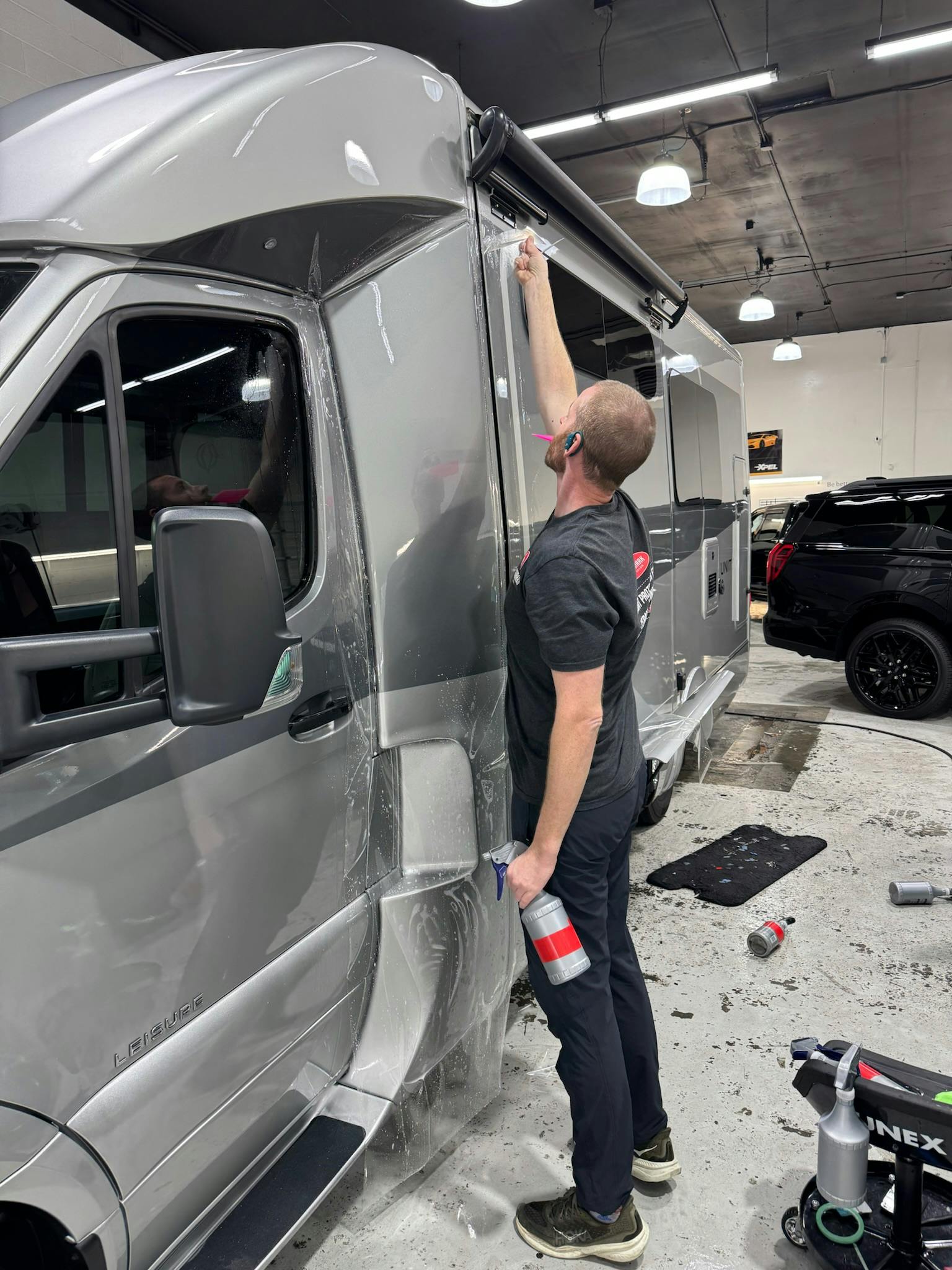 Installer applying XPEL paint protection film across the side of a Sprinter-based RV