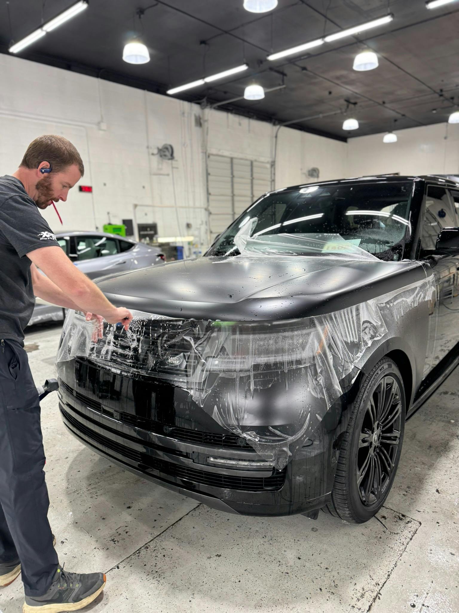 Benchmark installer wrapping the front bumper of a Range Rover in XPEL STEALTH PPF